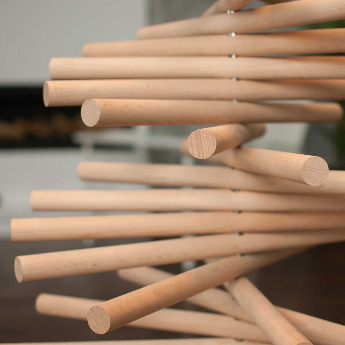 A minimalist wooden Christmas tree sculpture made from layered natural wood branches and small red ornaments, standing on a round wooden base against a plain white background.