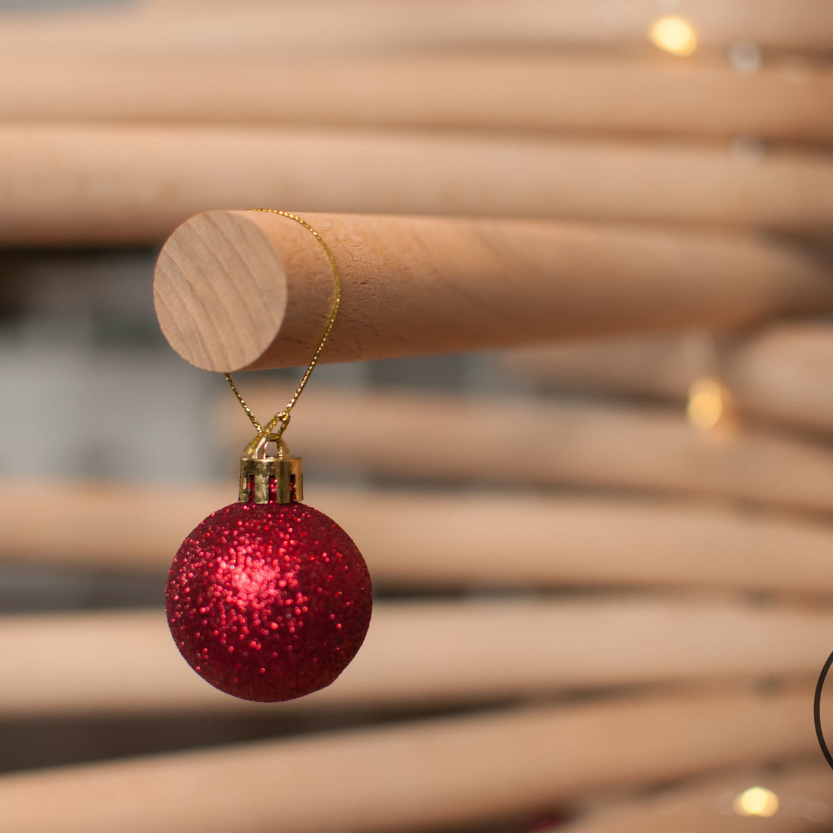 A minimalist wooden Christmas tree sculpture made from layered natural wood branches and small red ornaments, standing on a round wooden base against a plain white background.
